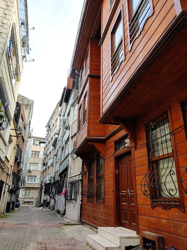 Une rue étroite en milieu urbain, bordée d’immeubles à plusieurs étages dotés de balcons et de fenêtres.
