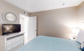 Ein Schlafzimmer mit einem Bett, einem Fernseher auf einer Kommode, einer Tür und einem an der Wand befestigten Spiegel.