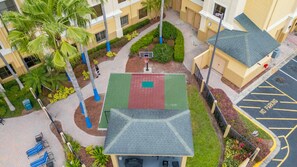 An aerial view of a courtyard with a basketball court, palm trees, and a building with a grey roof. - Harry Potter Apartment | Near Universal (Orlando)