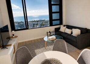 A modern living room with a large window, a sofa, a glass coffee table, and a TV. - 16 on bree (Cape Town)