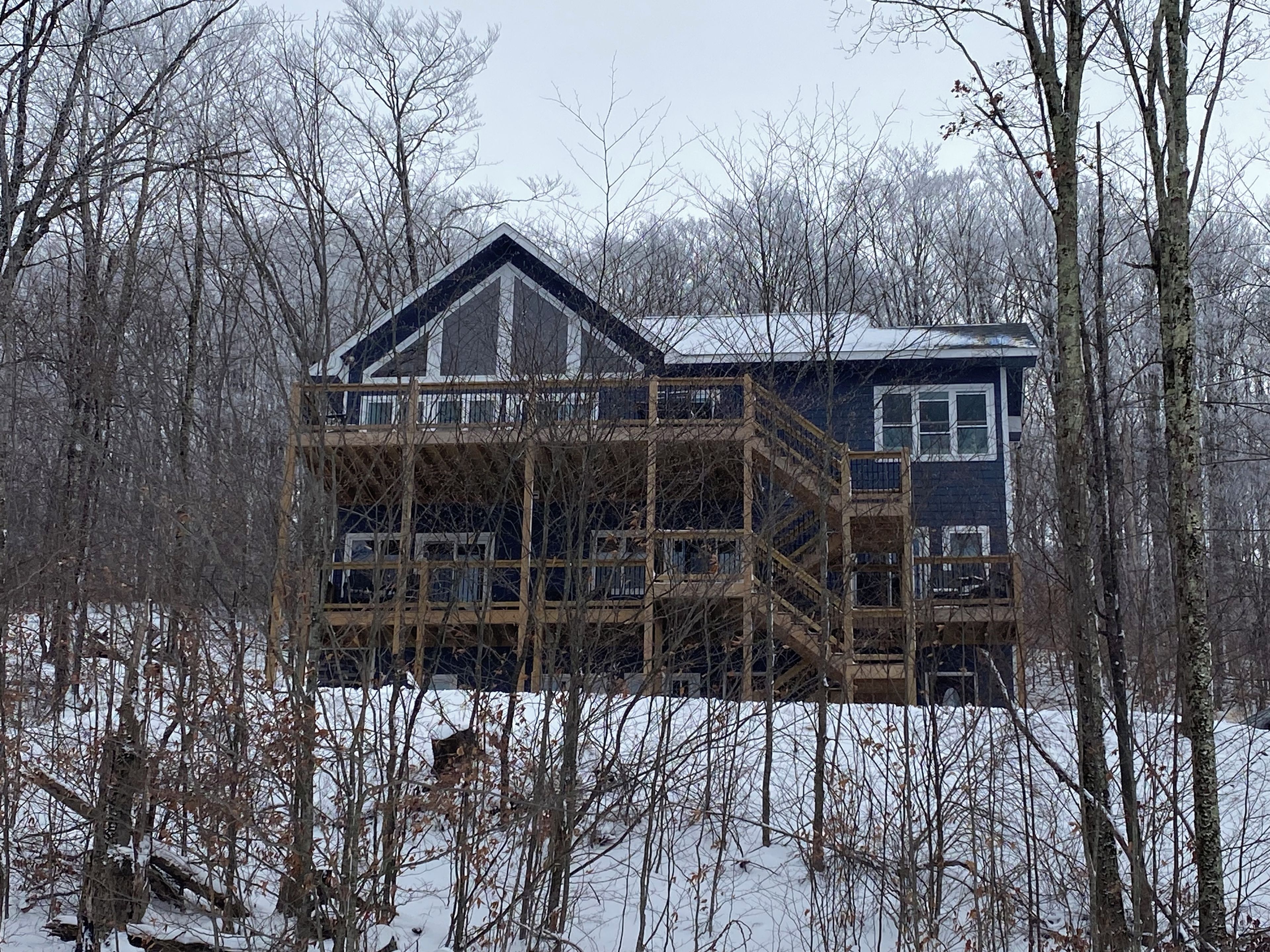 Una casa de dos pisos con una terraza de madera y un ventanal grande.
