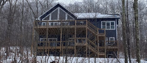 Ein zweistöckiges Haus mit einer Holzterrasse und einem großen Fenster.