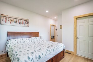Ein Schlafzimmer mit einem Bett, einem Holzkopfteil, einem Wandbild, einer Tür und einem Lichtschalter.