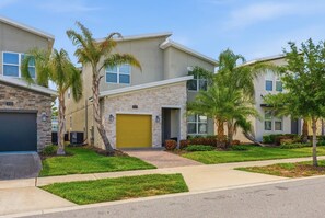 A modern residential building with a stone facade, a yellow garage door, and well-maintained landscaping including palm trees and grass. - 5-Bedroom Family House with Pool and Themed Rooms (Kissimmee)