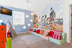 A room with a large wall mural, a sofa with colorful cushions, a play tent, and a television. - 5-Bedroom Family House with Pool and Themed Rooms (Kissimmee)