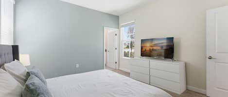 Une chambre à coucher avec un lit, un téléviseur posé sur un meuble, un ventilateur de plafond et une porte donnant sur une autre pièce.