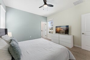 Una camera da letto con un letto, una TV su un mobile, una ventola a soffitto e una porta che dà su un'altra stanza.
