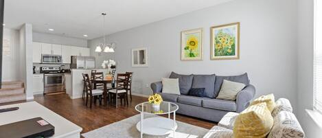 A modern living room with a grey sofa, a coffee table, and a dining area with a white table and chairs.