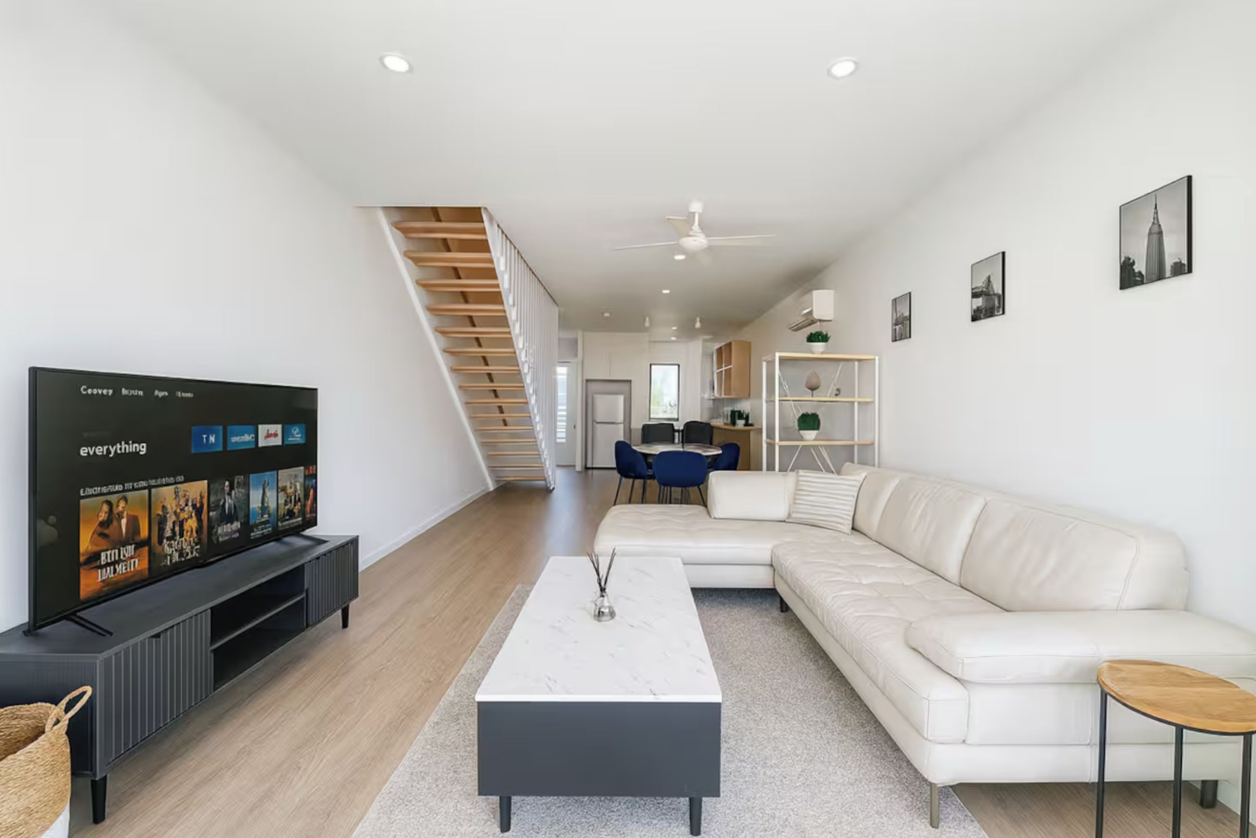 A modern living room with a flat-screen TV, a white sofa, a coffee table, and a staircase leading to another room.