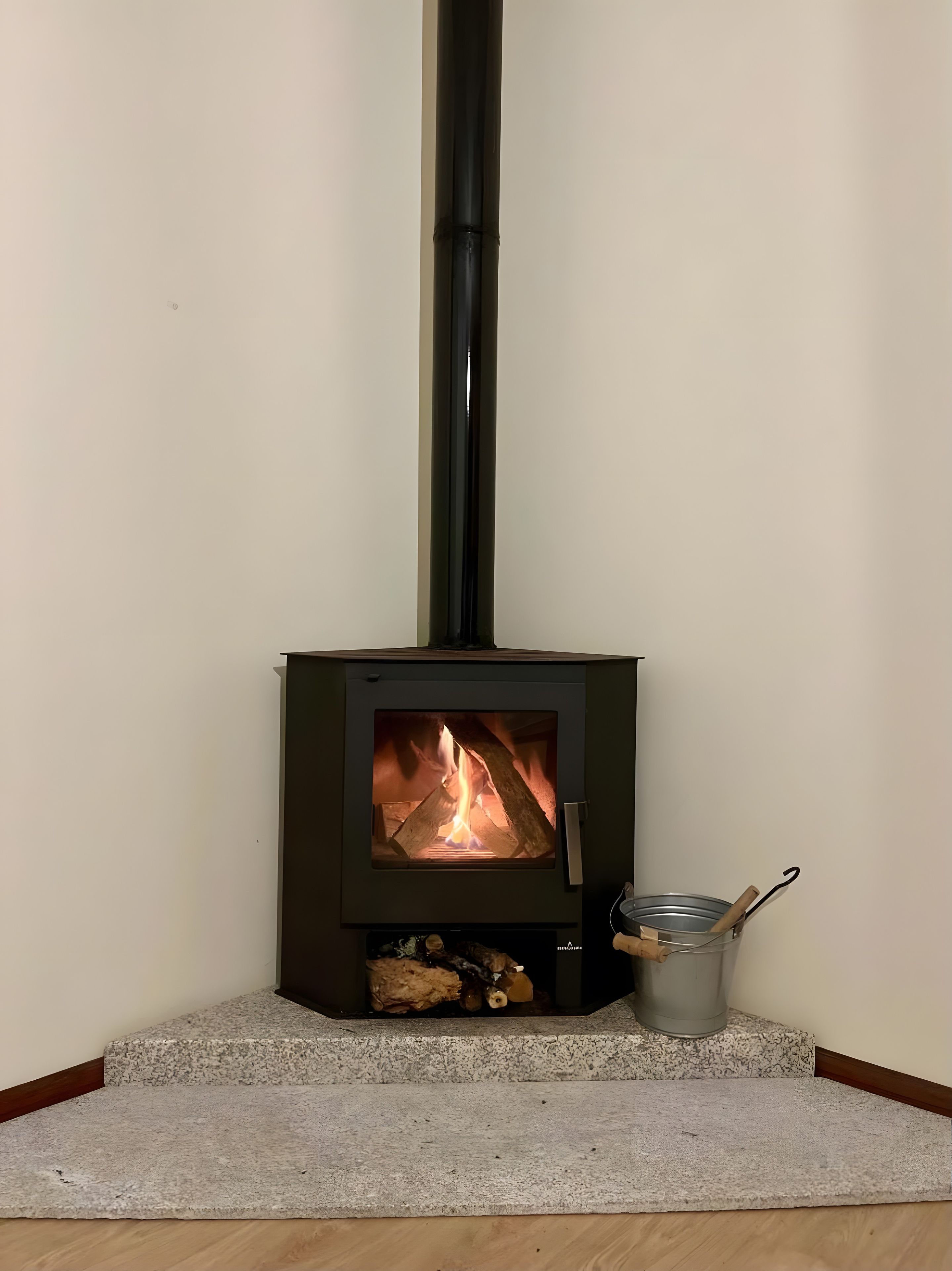 Una estufa de leña con fuego visible, un recipiente metálico con asa y una base de piedra.