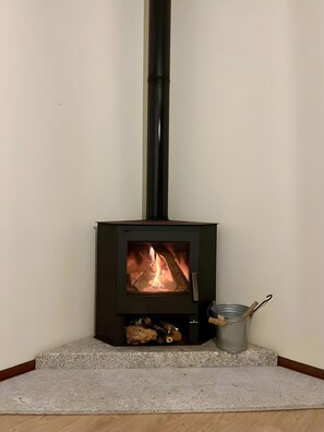 A wood-burning stove with a visible fire, a metal container with a handle, and a stone base.
