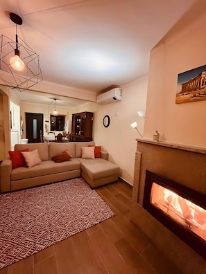 A living room with a fireplace, a patterned rug, a sofa, and a dining area in the background.