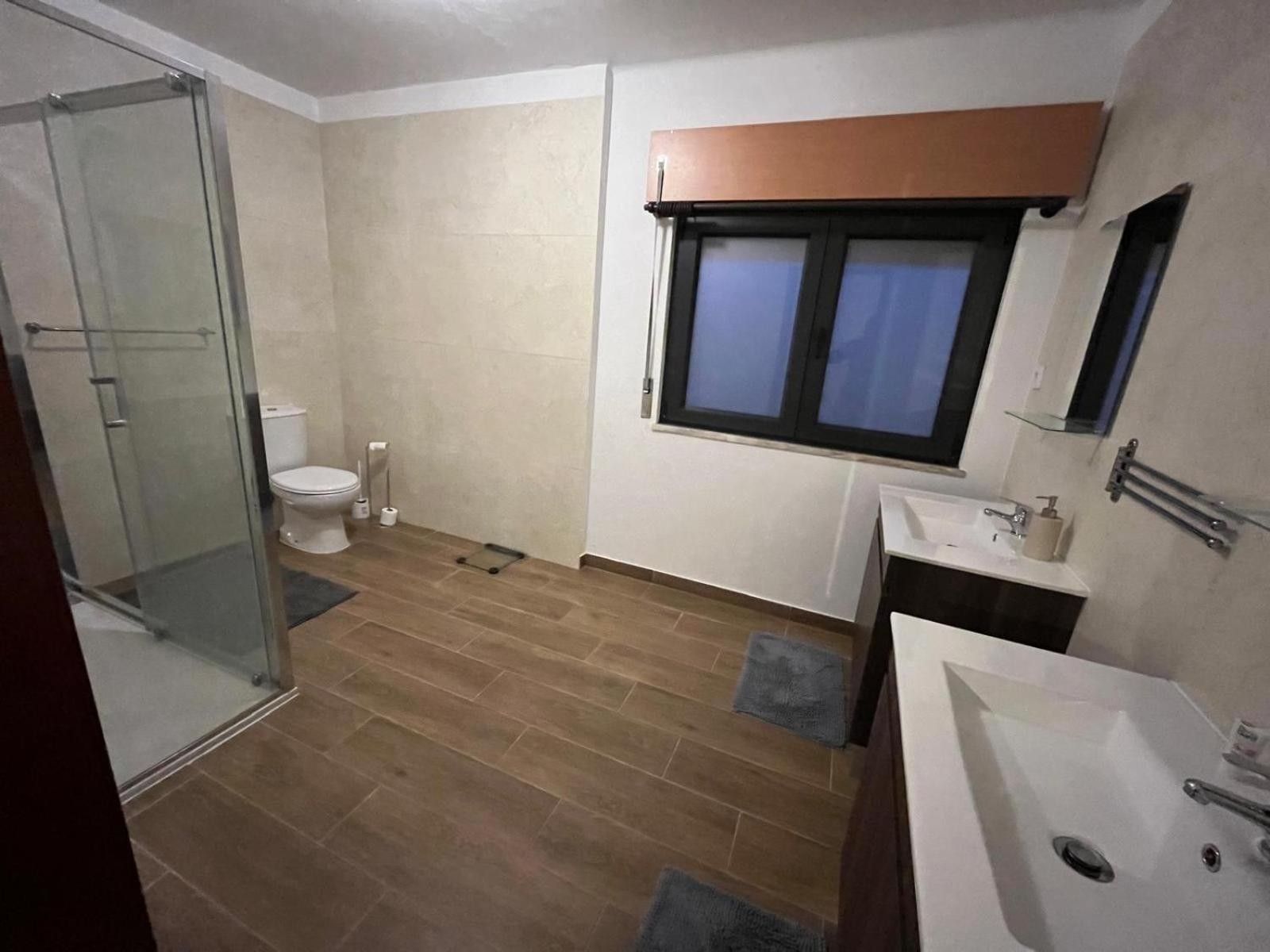 Une salle de bain avec une douche à parois de verre, des toilettes, un lavabo avec un miroir et une fenêtre avec un rideau.