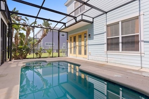 Piscina residencial con un porche cubierto, rodeada de una cerca y vegetación.