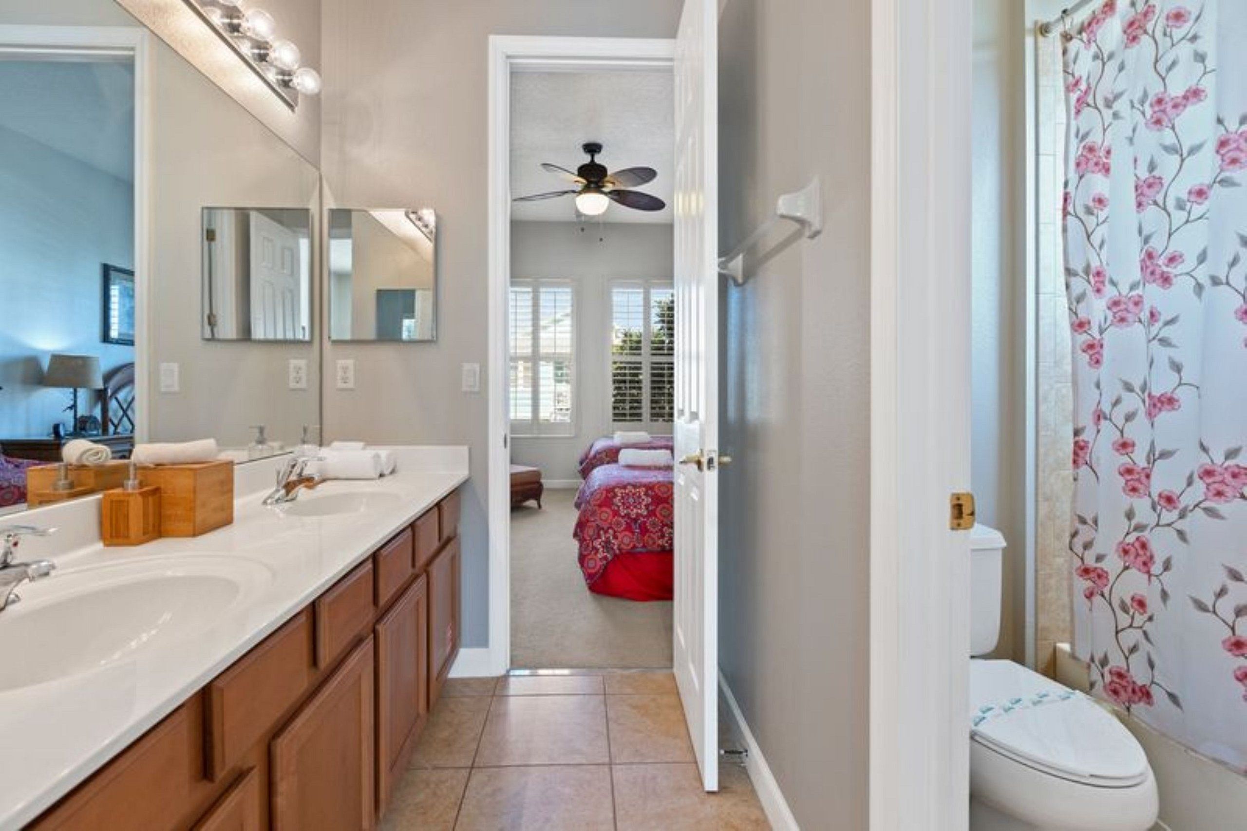 A bathroom with a white sink, wooden cabinets, a mirror, and a toilet with floral wallpaper.