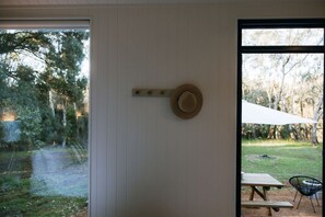 A room with a large window, a hat on the wall, a wooden bench, and a chair outside.