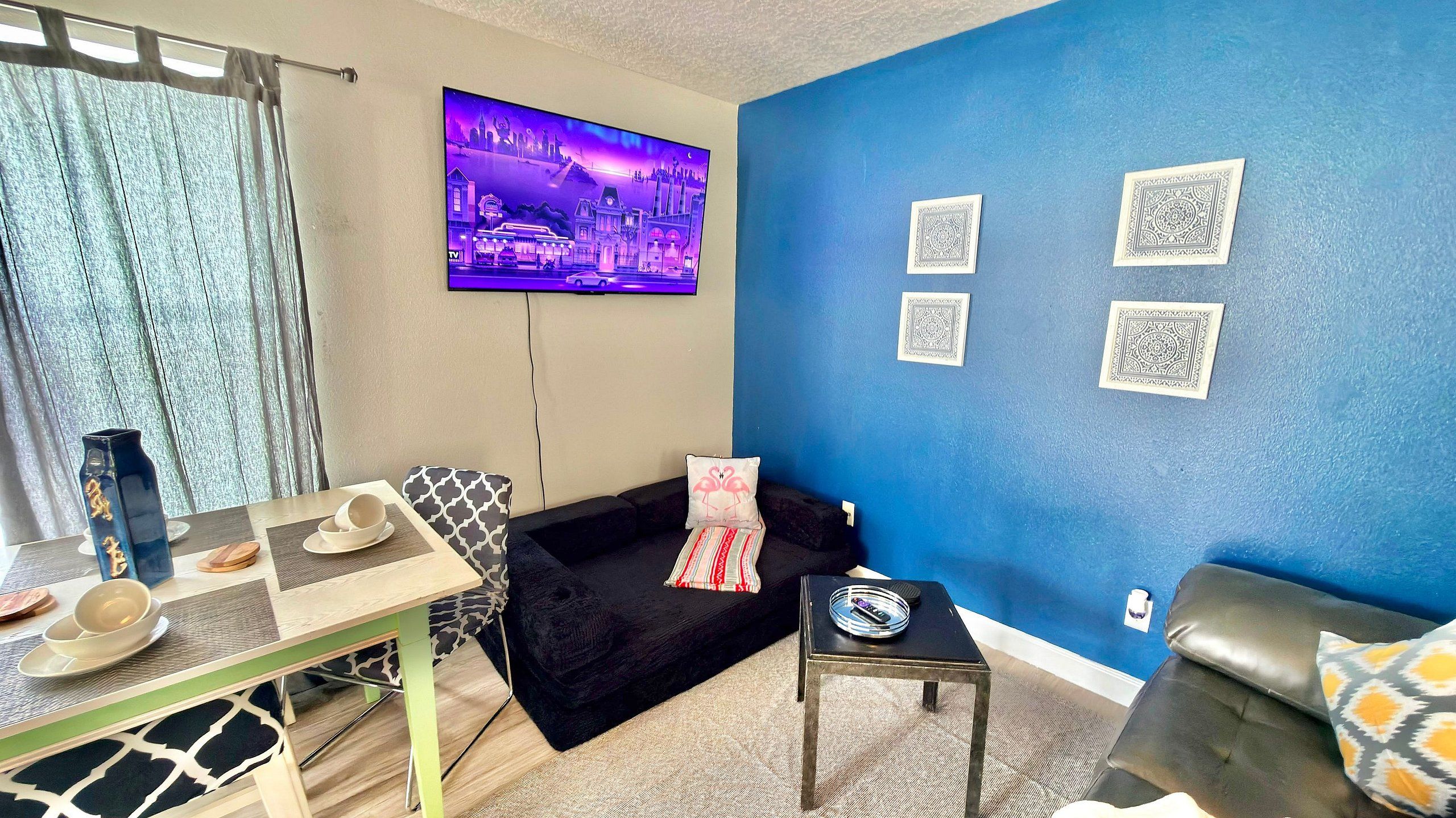 Una sala de estar con televisor, sofá, mesa de centro y pared azul con diseños decorativos.