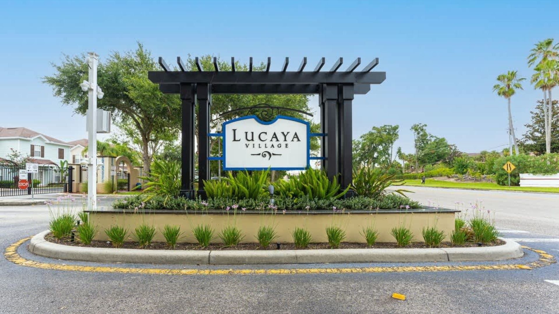 A sign for Lucaya Village with a pergola structure and a landscaped area with small plants.