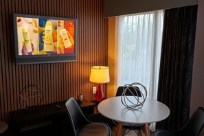 A hotel room with a television displaying Dove products, a round table with chairs, a red lamp, and a window with curtains. - 2BR Condo Near Universal & I-Drive Attractions (Orlando)