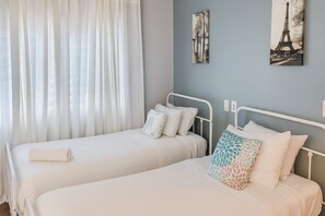 A hotel room with two single beds, a window with sheer curtains, and two wall-mounted artworks. - 2BR Condo Near Universal & I-Drive Attractions (Orlando)