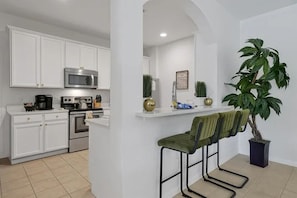 A modern kitchen with white cabinetry, stainless steel appliances, and a bar area with stools. - 5BR Home Near Disney with Pool & Game Room (Kissimmee)