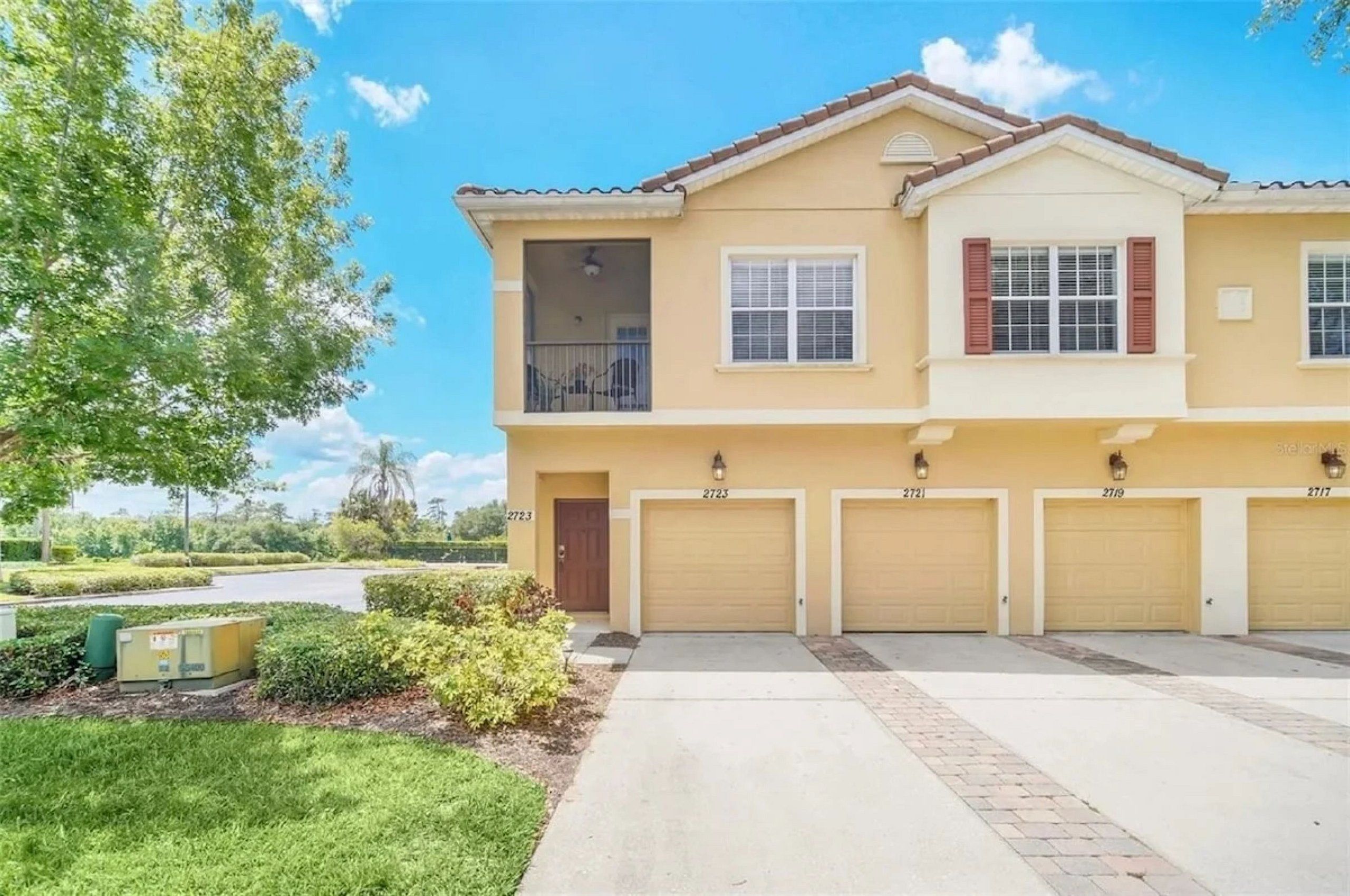 A two-story residential building with a garage, a balcony, and a well-maintained lawn.