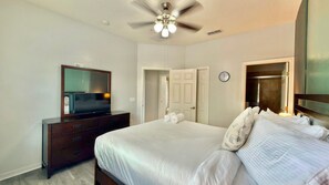 Habitación de hotel con cama, cómoda, televisor, ventilador de techo y reloj en la pared.