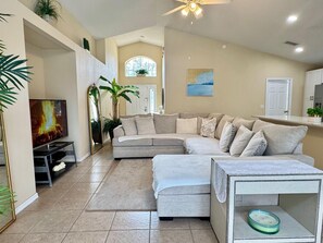 A living room with a sectional sofa, a flat-screen TV, a ceiling fan, and a large window. - Lake Berkley 3BR – Disney 10min, Pool & Lake (Kissimmee)
