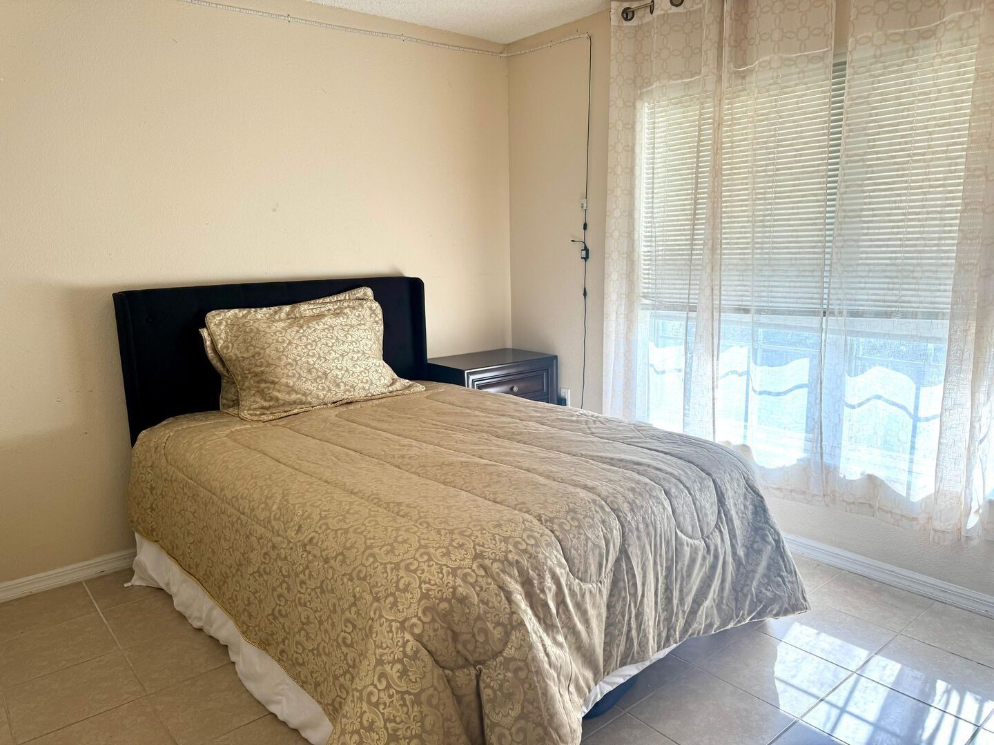 Une chambre à coucher avec un lit, une table de chevet, une fenêtre avec des stores et un rideau.