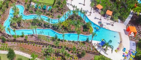 An aerial view of a resort with a winding pool, palm trees, and a children's play area.