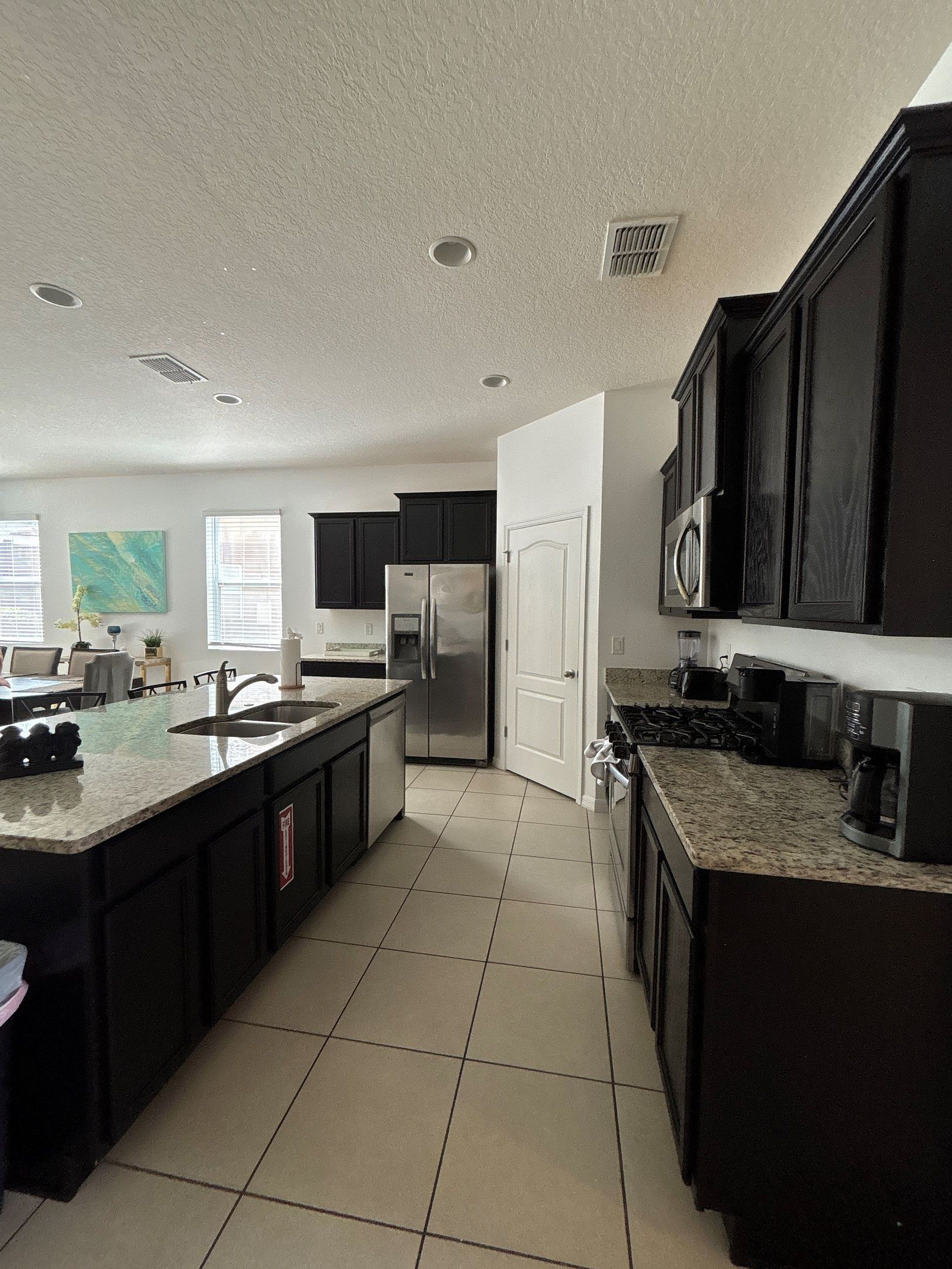 A modern kitchen with a central island, dark cabinetry, stainless steel appliances, and a tiled floor.