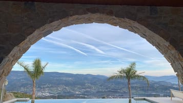 An infinity pool with a clear view of a mountainous landscape through a stone archway.