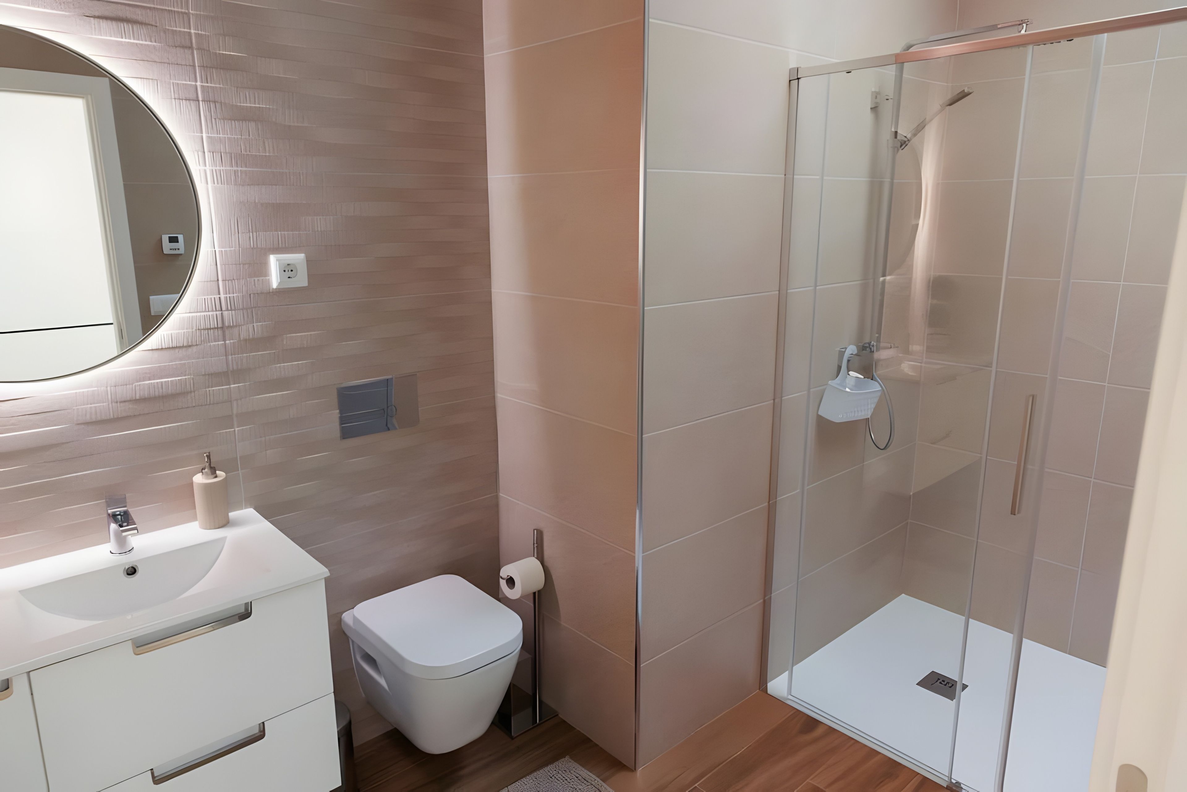 Un baño moderno con lavamanos blanco, inodoro y ducha con cerramiento de vidrio.