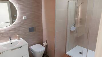 Un baño moderno con lavamanos blanco, inodoro y ducha con cerramiento de vidrio.