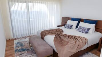 Une chambre à coucher avec un lit, un banc, une table de chevet et une fenêtre avec des stores.