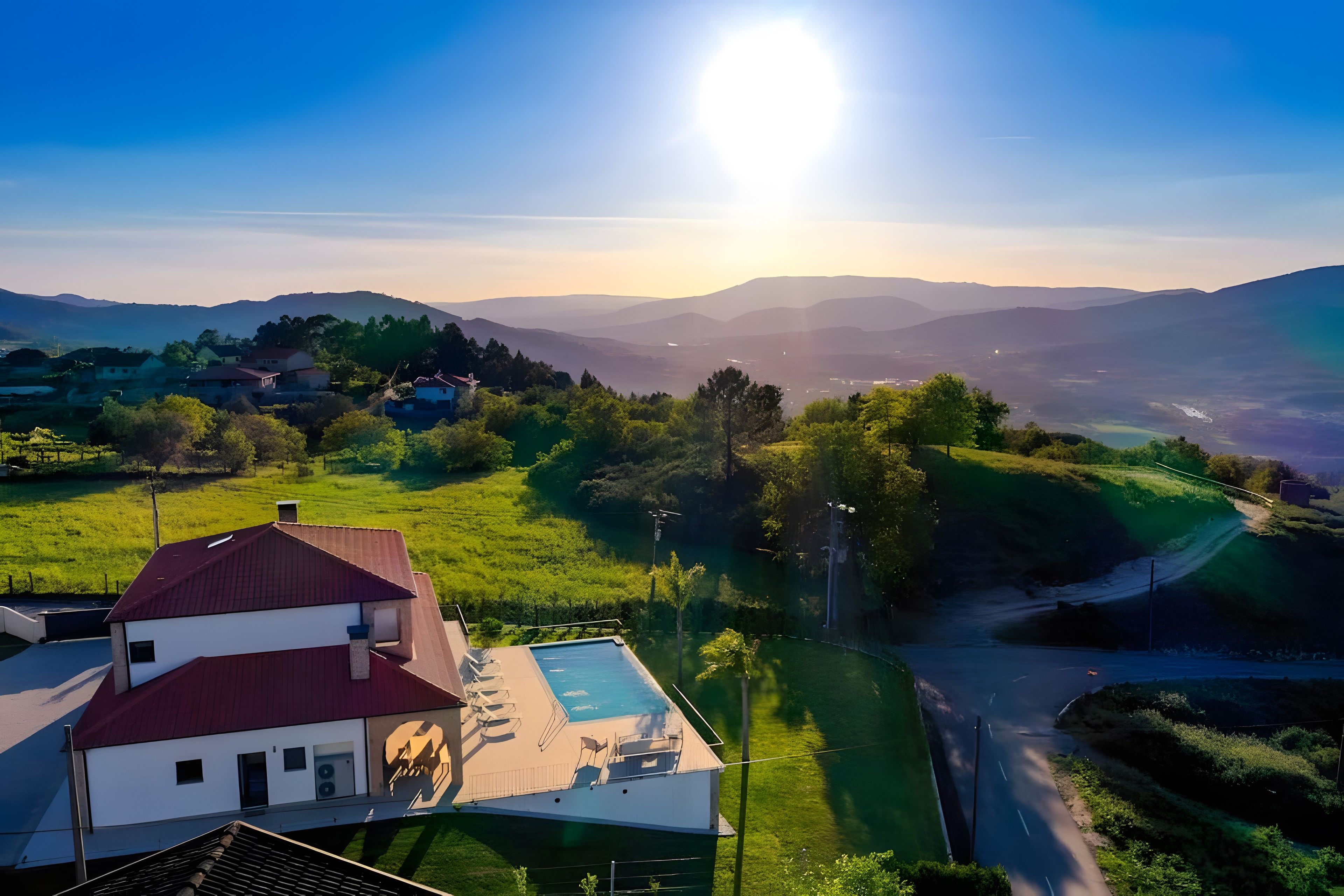 A residential area with a house featuring a swimming pool, surrounded by lush greenery and distant mountains.