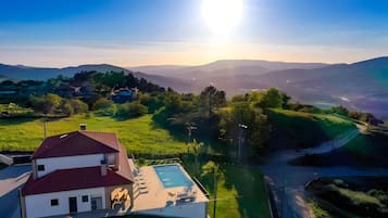 A residential area with a house featuring a swimming pool, surrounded by lush greenery and distant mountains.
