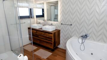 Une salle de bain moderne dotée d’une douche à parois de verre, d’un meuble-lavabo en bois avec deux vasques, d’une grande baignoire et d’un mur orné d’un motif en chevrons.