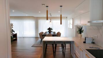 Una cocina moderna con zona de comedor, suelo de madera, luces colgantes y una planta en maceta.