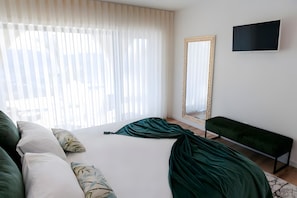 Un dormitorio con cama, un banco, televisor y un ventanal con persianas.