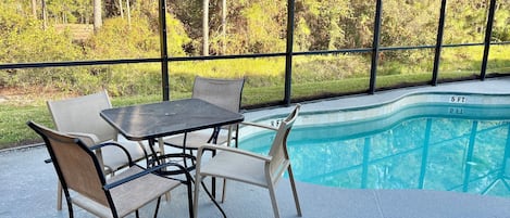 An outdoor patio with a pool, surrounded by a metal fence, and furnished with a table and chairs.