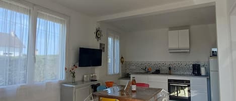 A compact kitchen with a dining area, a flat-screen TV mounted above the counter, and a view of the outside through the window.