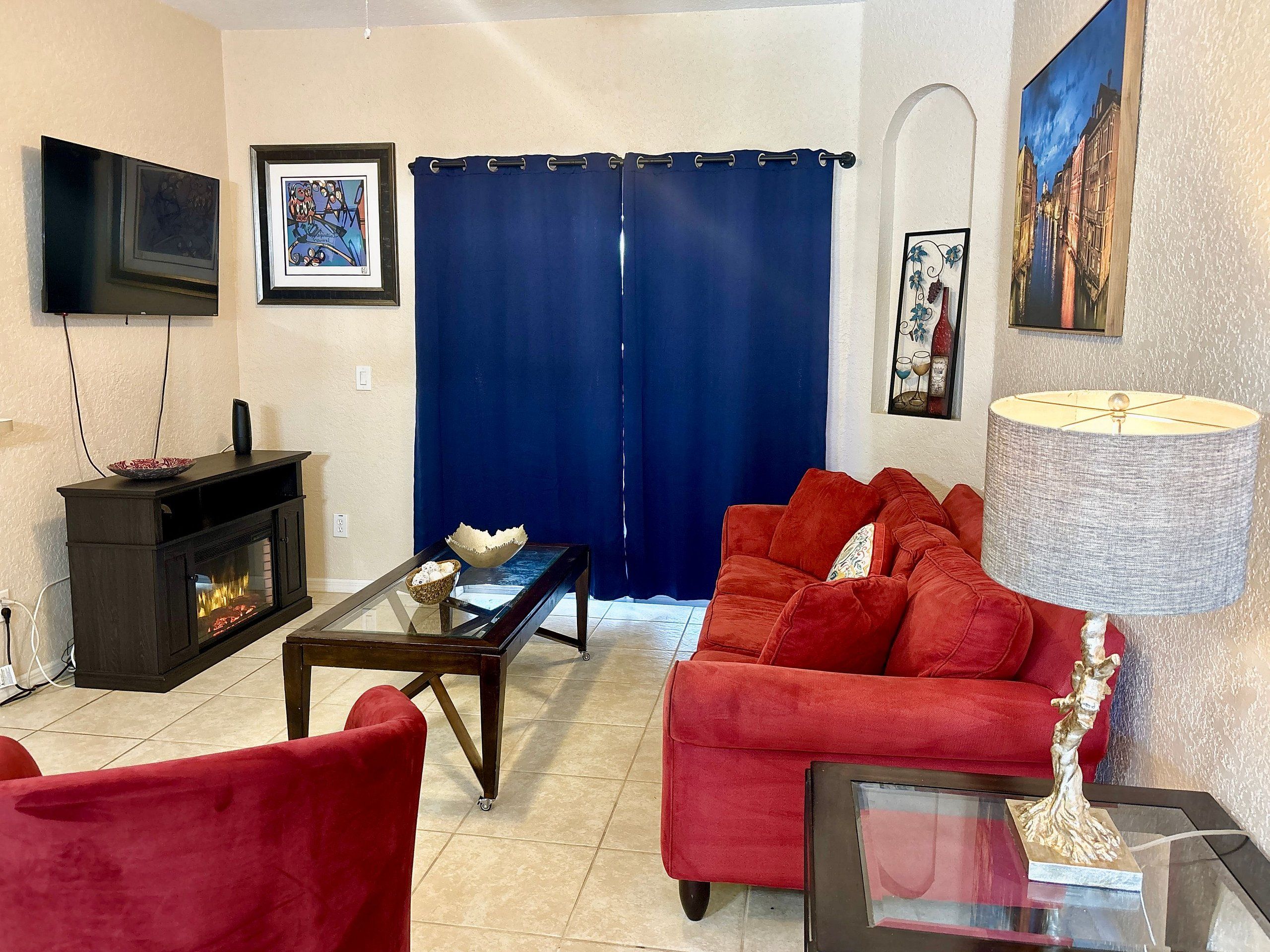A living room with a fireplace, red sofa, and a television mounted on the wall.