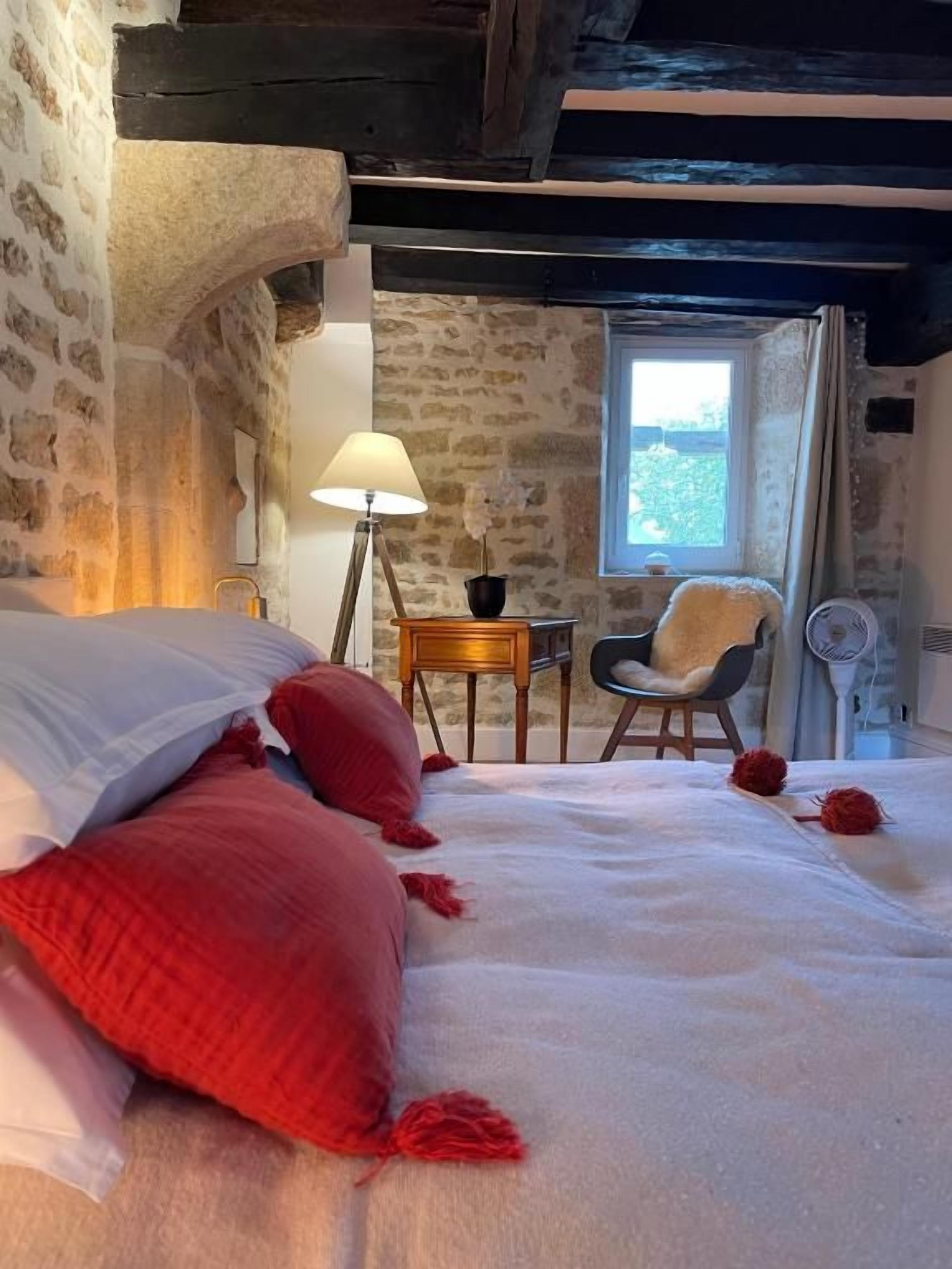 A bedroom with a bed, pillows, a lamp, a chair, and a window.