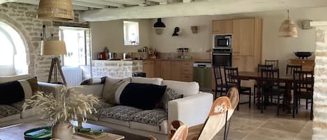 Amplia sala de estar con sofá, mesa de comedor y sillas, una cocina con electrodomésticos modernos y una pared de piedra.