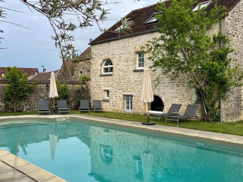 A swimming pool with lounge chairs and umbrellas, surrounded by stone buildings with windows and a clear sky.