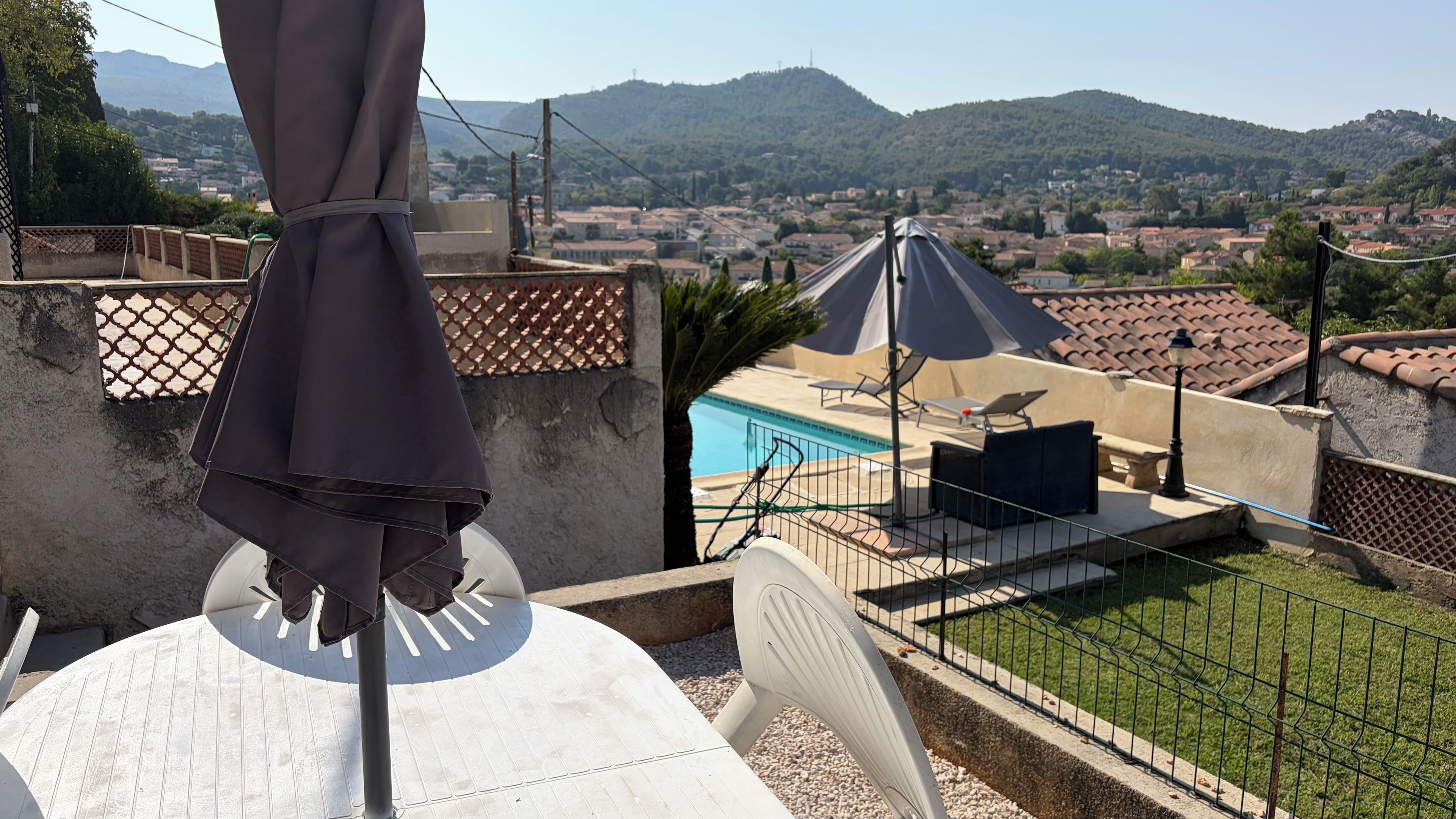 Una terraza con piscina, mobiliario exterior y vistas a un pueblo y montañas.