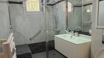 A modern bathroom with a glass shower enclosure, a white sink, and a toilet.