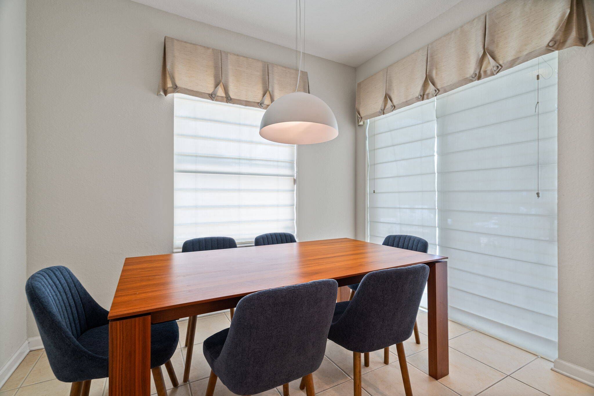 Un comedor con una mesa de madera y seis sillas, una lámpara colgante y una ventana con persianas.