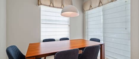 Un comedor con una mesa de madera y seis sillas, una lámpara colgante y una ventana con persianas.
